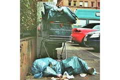 A shopping cart filled with trash on top of a pile of trash bags.